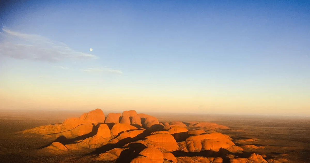 The domes of Kata Tjuta lit orange at sunrise, seen from the air above the plain
