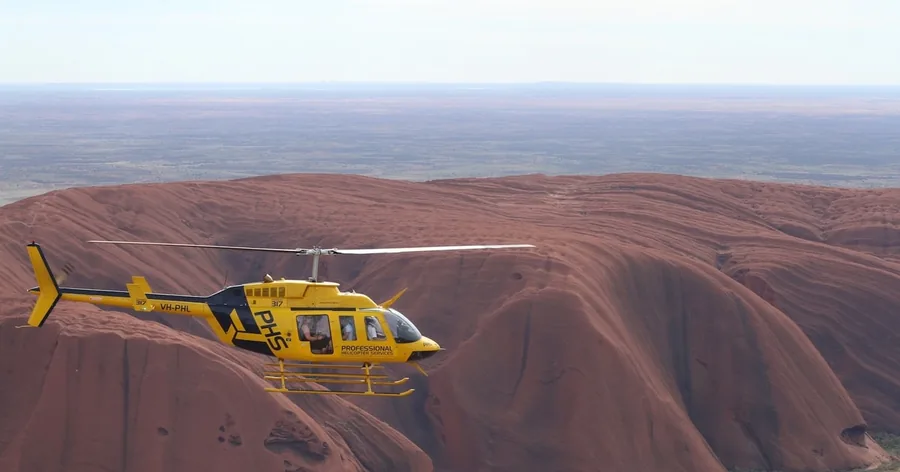 A yellow helicopter flying over the rippled red top of Uluru