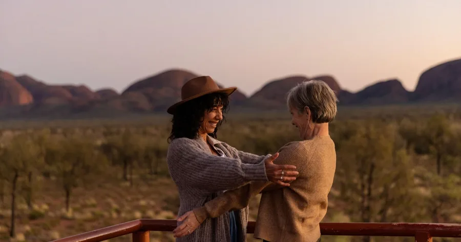 Two women laughing on a viewing platform with the domes of Kata Tjuta behind them at dusk